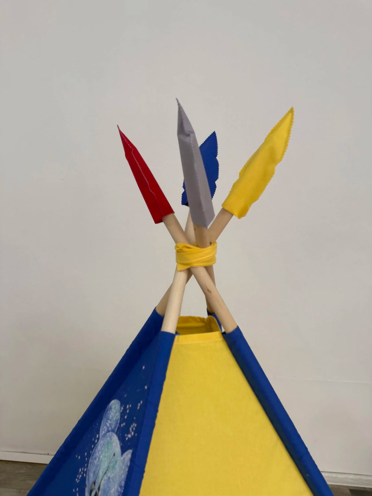 Dettaglio piume tenda teepee bambini in rosso, grigio, blu e giallo, pali legno naturale e decorazione artigianale