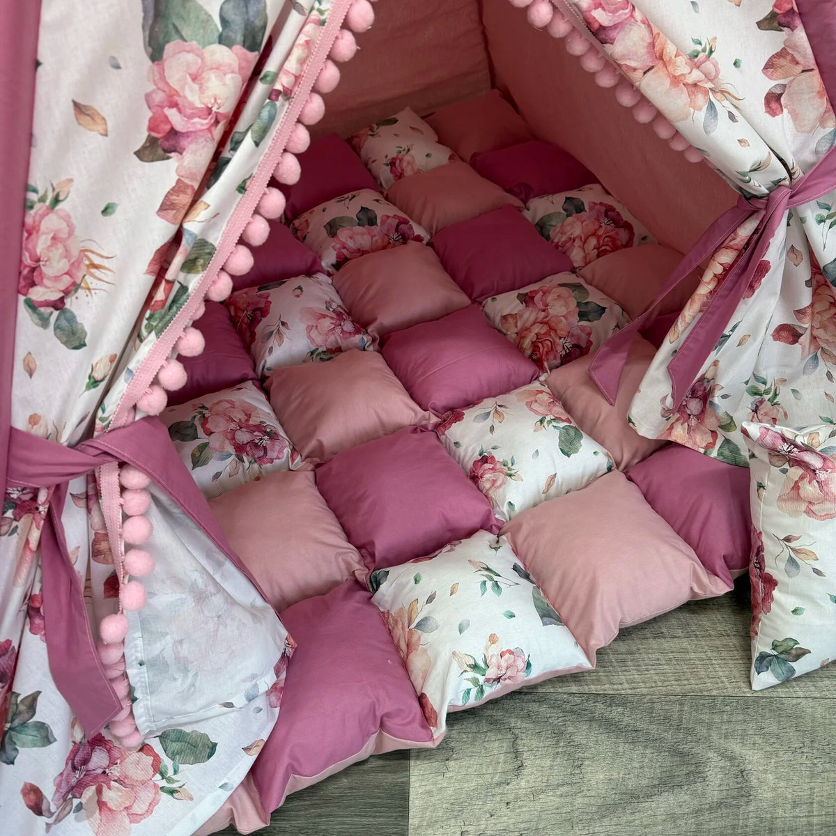 Interno tenda teepee bambini con tappeto rosa antico e pastello a scacchi, decorazioni floreali e pompon