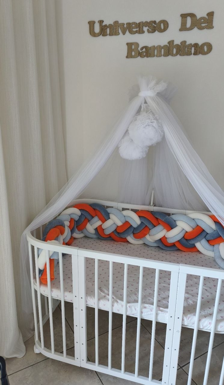 Treccia paracolpi a 8 fili multicolore arancio e azzurro su lettino ovale bianco, vista laterale