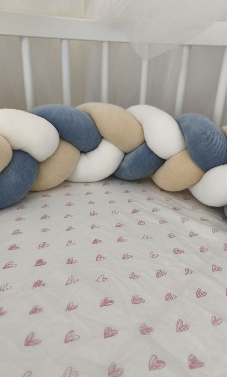Dettaglio della treccia paracolpi blu polvere, beige e bianco fissata alle sbarre del lettino