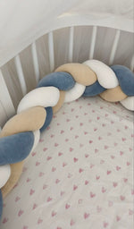 Treccia paracolpi blu polvere, beige e bianco montata lungo le sponde arrotondate di un lettino ovale