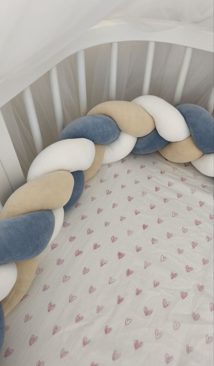 Treccia paracolpi blu polvere, beige e bianco montata lungo le sponde arrotondate di un lettino ovale