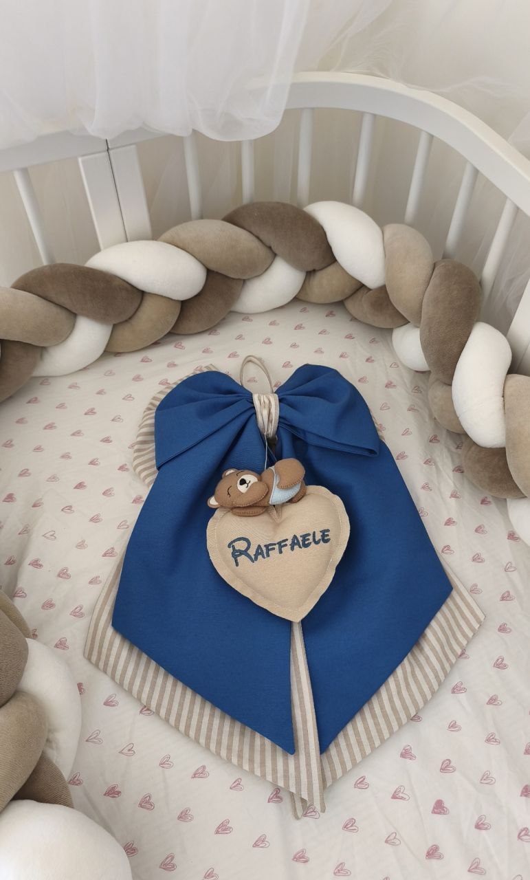 Fiocco nascita blu con cuore personalizzato con nome Raffaele e orsetto, dentro un lettino ovale con treccia paracolpi cappuccino, tortora e bianco