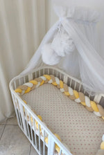 Lettino con treccia paracolpi giallo, beige e bianco e velo baldacchino bianco nella cameretta