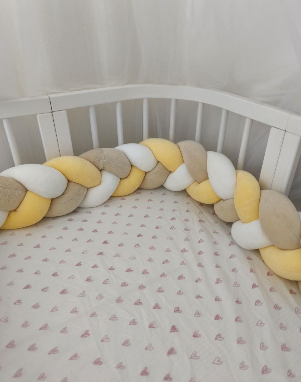 Treccia paracolpi giallo, beige e bianco montata lungo le sponde arrotondate di un lettino ovale