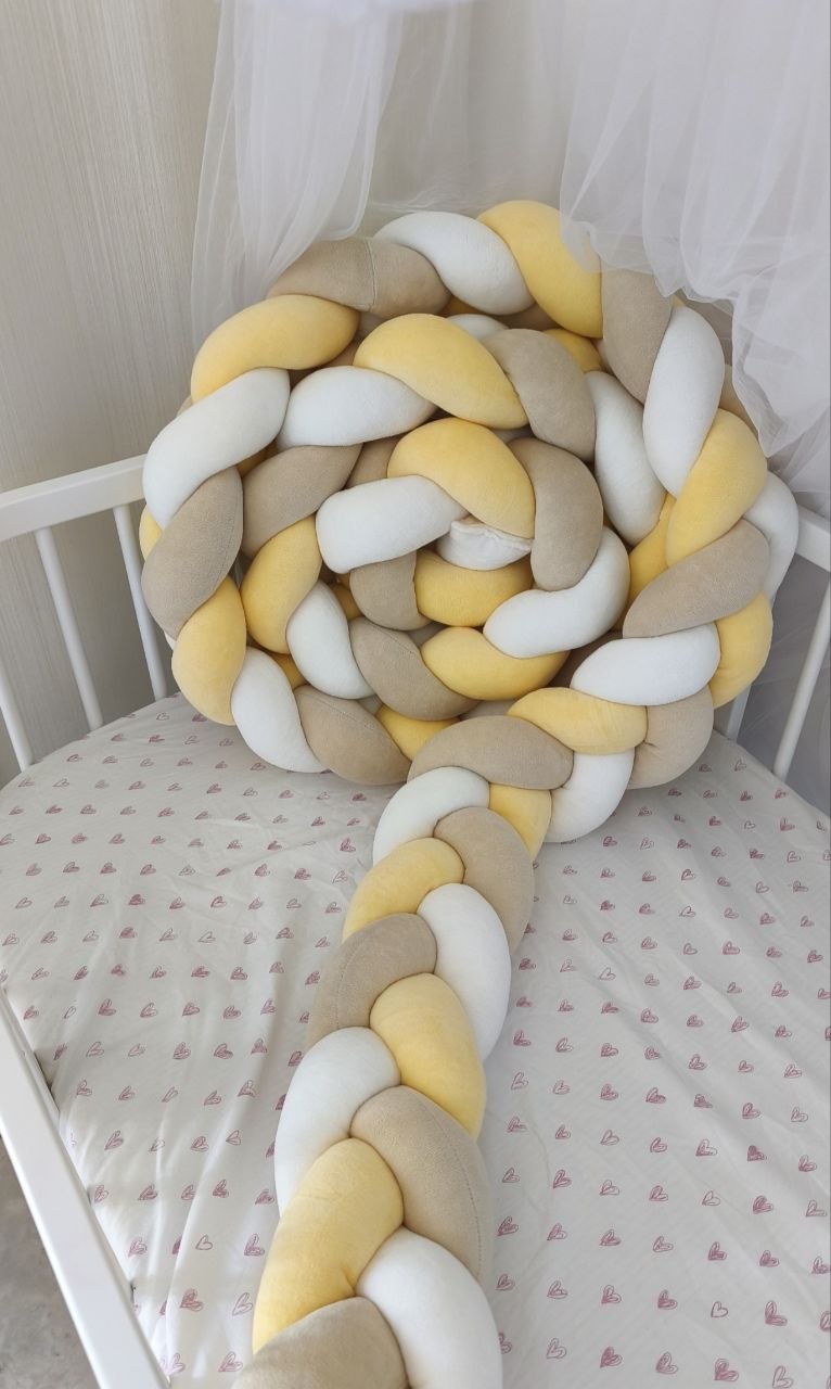 Treccia paracolpi a 3 fili giallo sole, beige classico e bianco in velluto, avvolta dentro un lettino ovale bianco