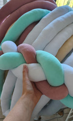 Mano su trecce paracolpi in velluto menta, rosa antico e bianco, dettaglio della morbidezza dell'imbottitura