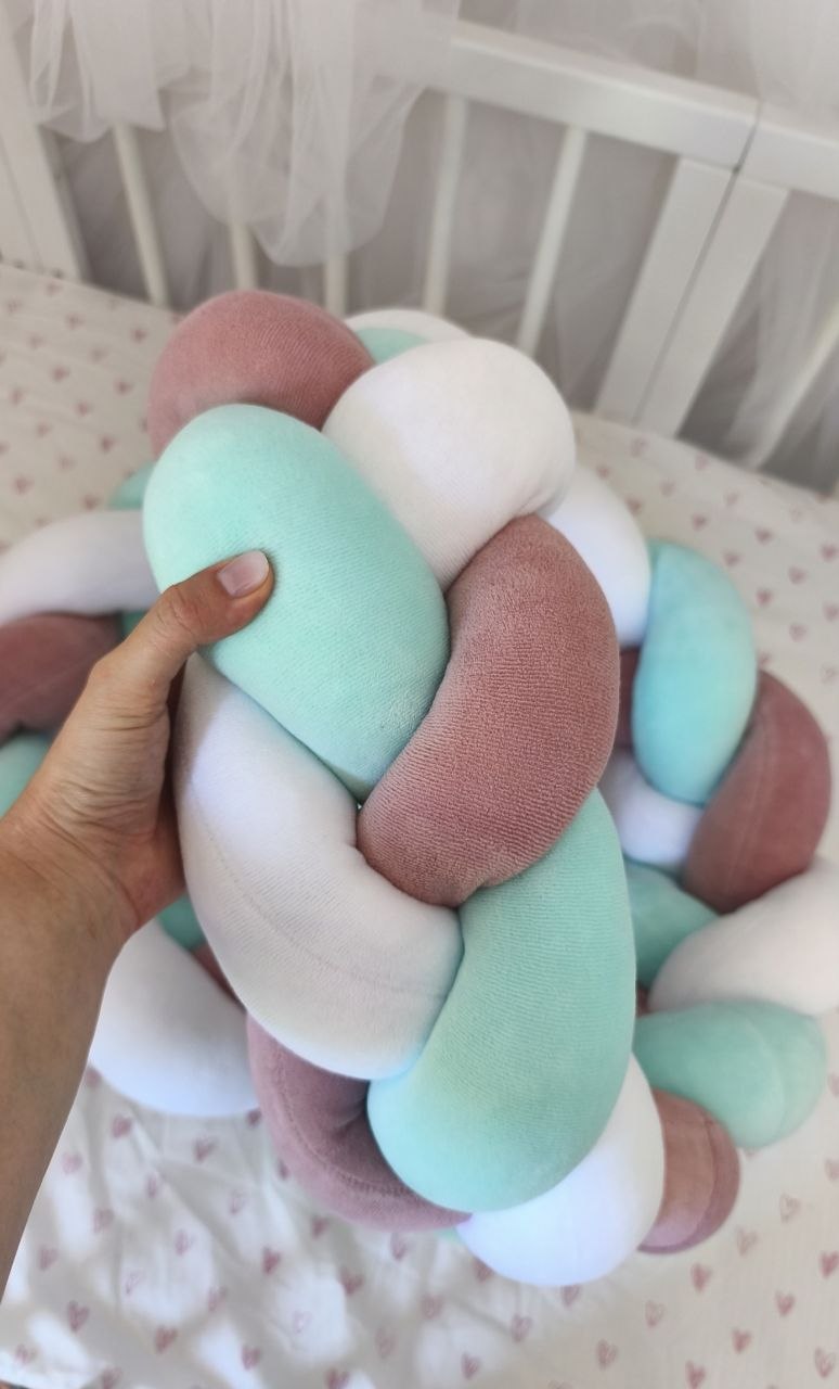 Mano che tiene la treccia paracolpi a 3 fili menta, rosa antico e bianco in velluto, dettaglio dell'intreccio morbido