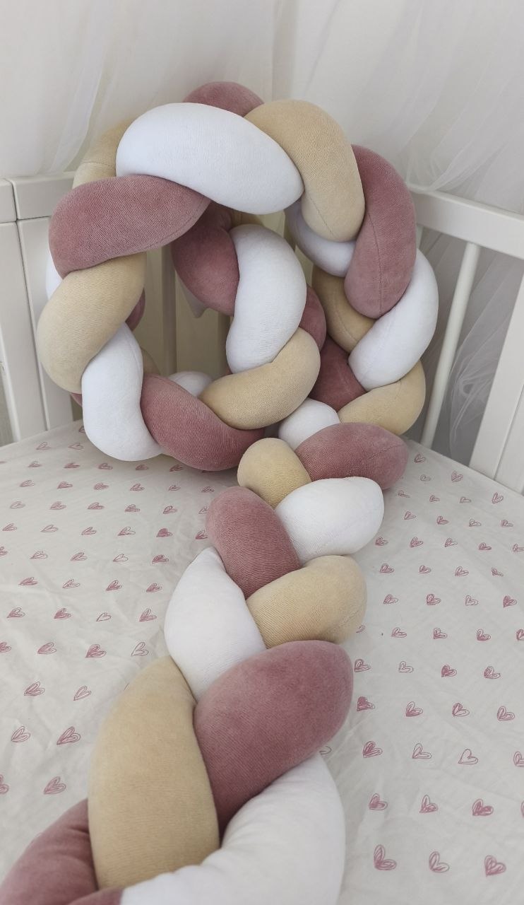 Intreccio della treccia paracolpi rosa antico, beige e bianco distesa sul materasso del lettino