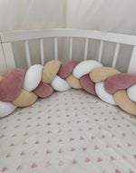 Treccia paracolpi rosa antico, beige e bianco montata lungo le sponde di un lettino ovale bianco