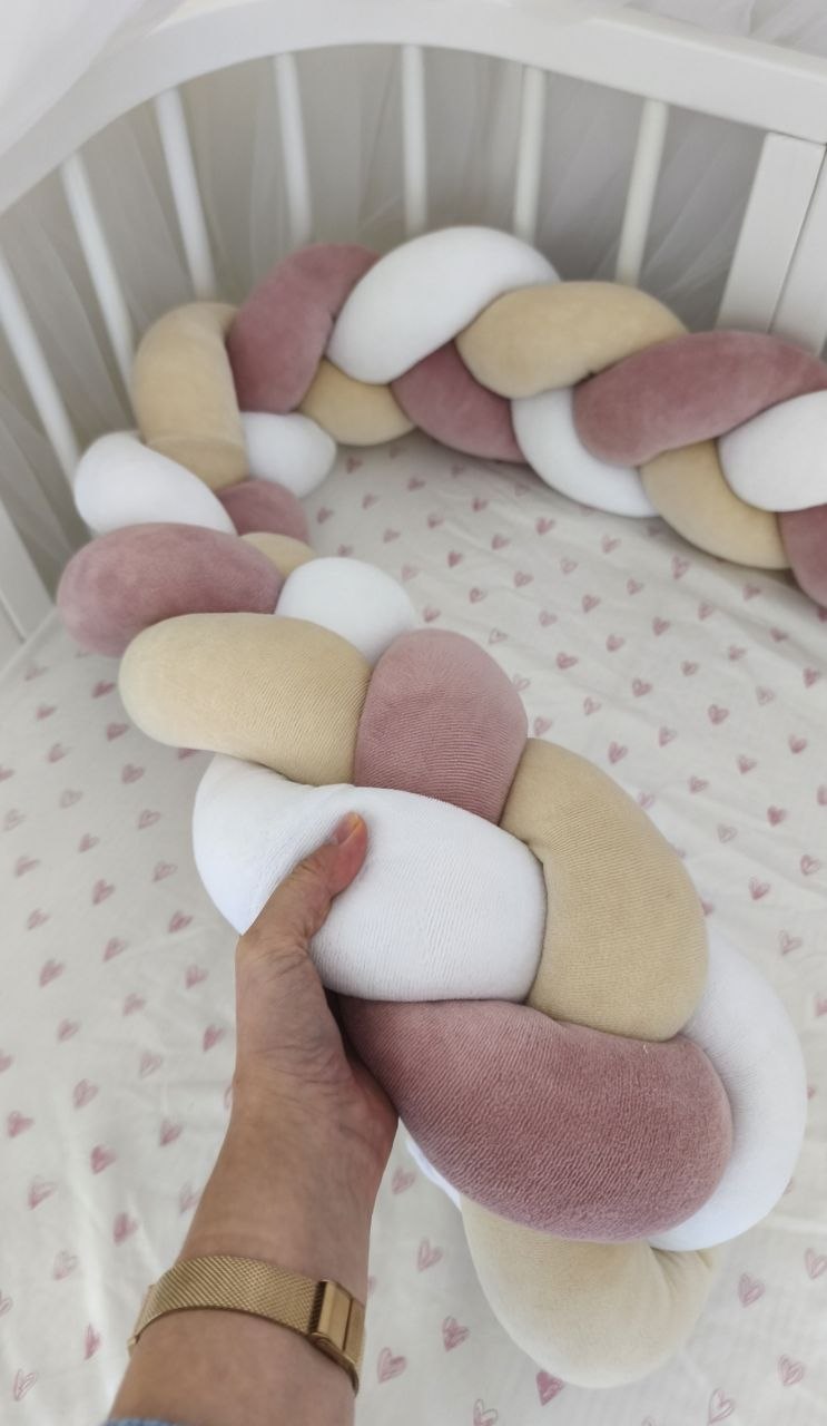 Mano che stringe la treccia paracolpi rosa antico, beige e bianco per mostrare la morbidezza dell'imbottitura