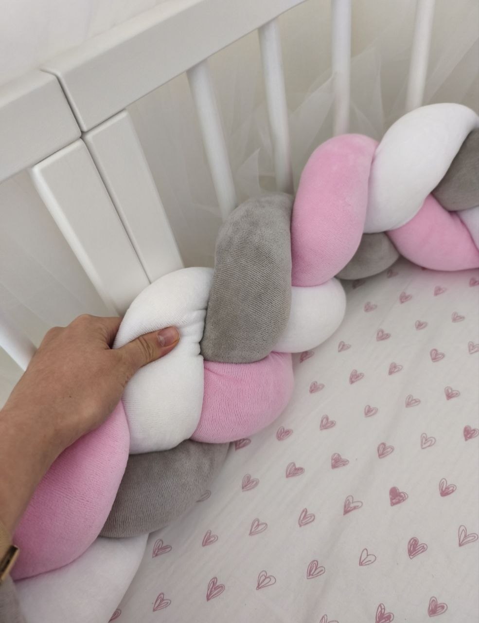 Treccia paracolpi rosa baby, grigio e bianco sistemata lungo le sbarre del lettino bianco