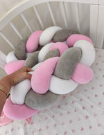 Mano che tiene la treccia paracolpi a 3 fili rosa baby, grigio classico e bianco in velluto, dettaglio dell'intreccio morbido nel lettino