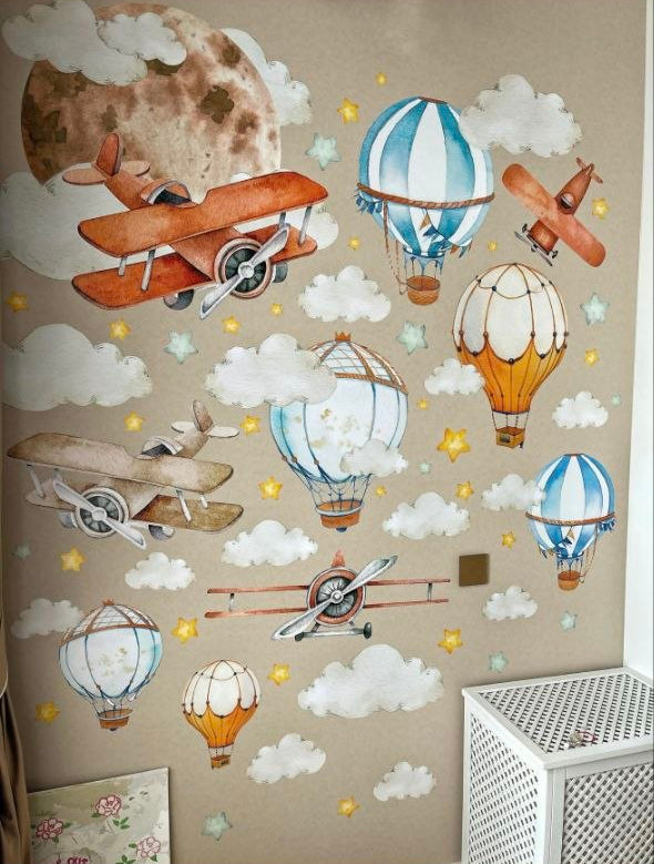 Decorazione parete cameretta con adesivi di aerei vintage, mongolfiere e una grande luna piena su sfondo tortora chiaro.